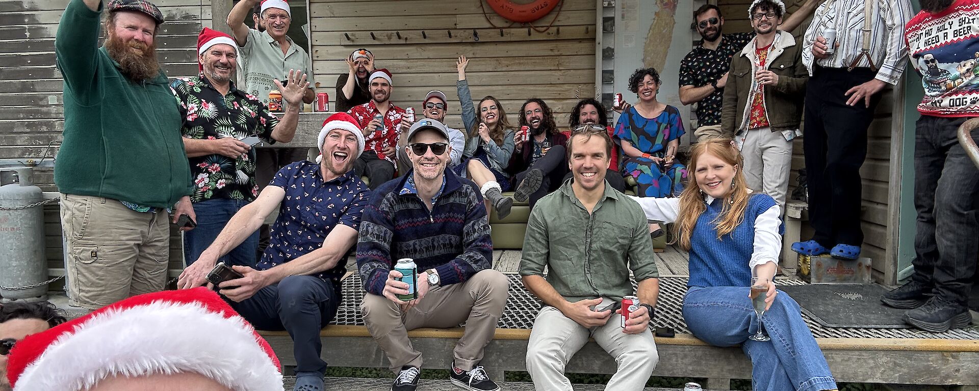 A group of men and women sitting on the steps with some wearing Christmas hats