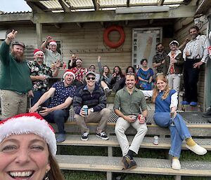 A group of men and women sitting on the steps with some wearing Christmas hats