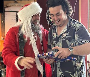 A man dressed in a red Santa suit with another man with a gift or present