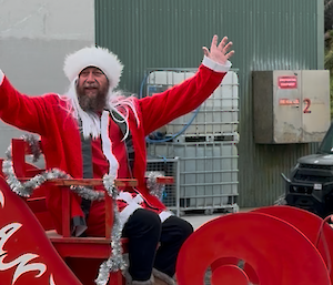 A man dressed as Santa sitting on a red sleigh