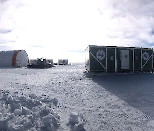 Panoramic view of an ice core camp site with a row of shipping containers and a large cylindrical tent.