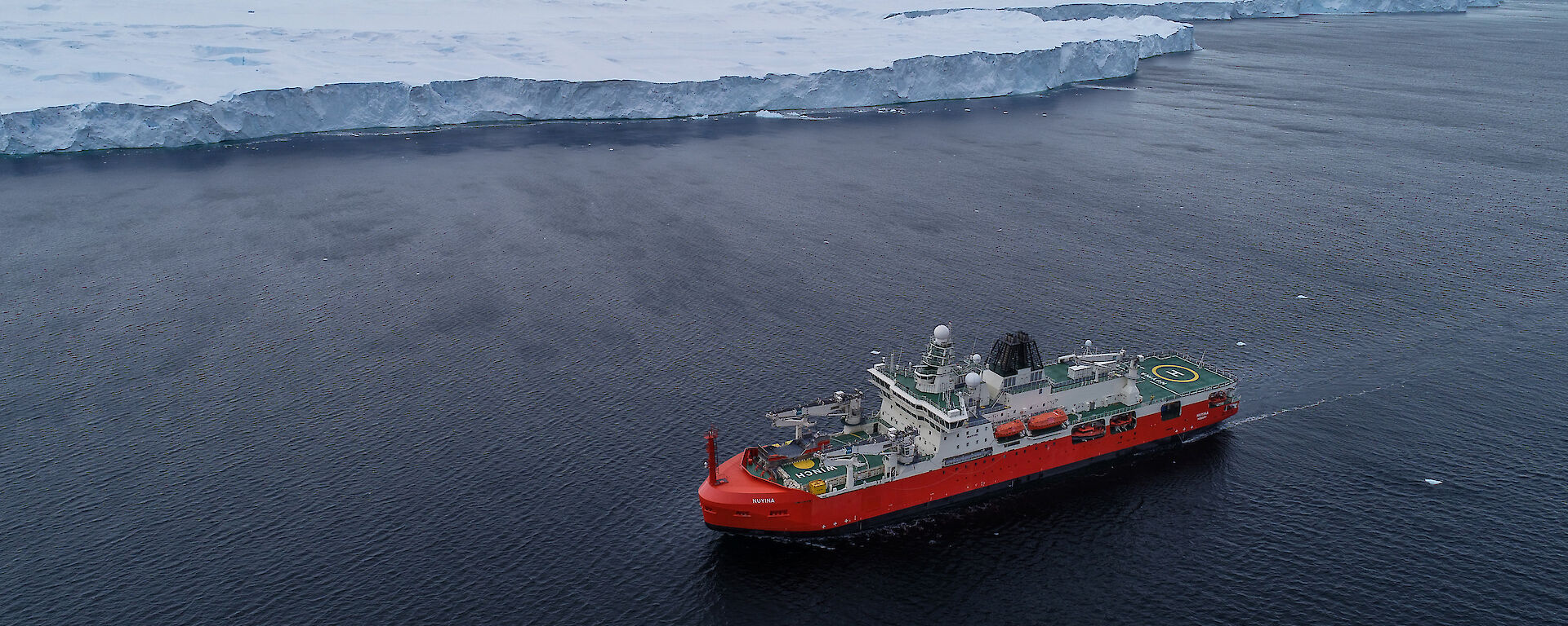 A red and white ship sailing past a vast white ice shelf
