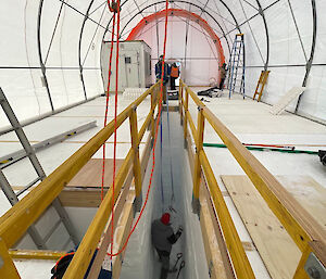 A person inside a narrow trench, inside a large tent.