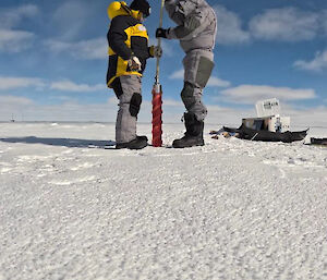 Two people with a hand-held ice drill, taking a core from the ice.