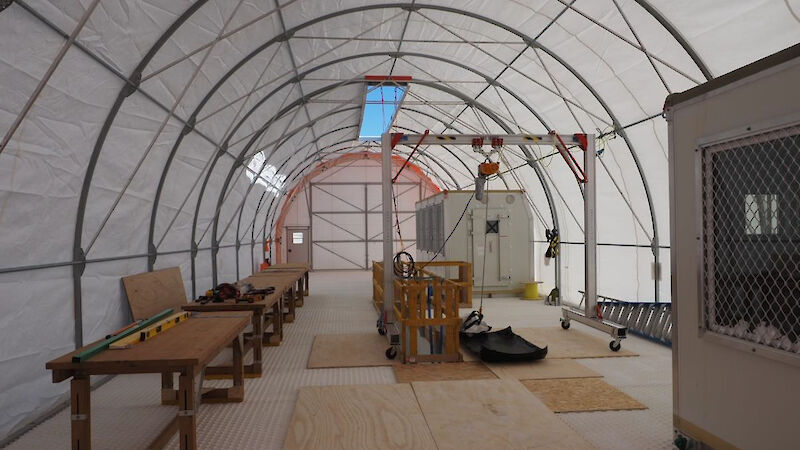 Wooden benches and plywood floor coverings set up inside a large tent.
