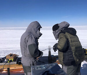 Two people in warm, grey suits hold a piece of metal cable.
