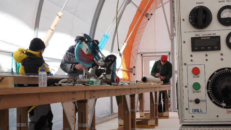 Three people working at a wooden bench inside a large tent.