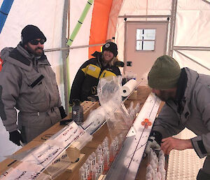 Three people labelling plastic bags and tubes on a wooden bench.