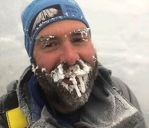 A man wearing a beanie and warm clothes with snow and ice sticking to his eyebrows, beard and moustache