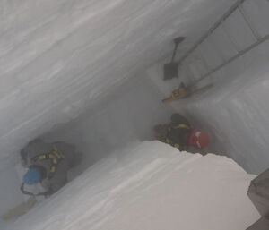 Two people in a narrow six-metre deep trench, with shovels and a ladder