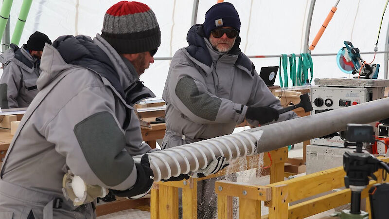 Two men remove an ice core from a drill barrel