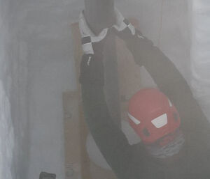 A man in the bottom of the ice drill trench guiding a metal cylinder in to a drill hole