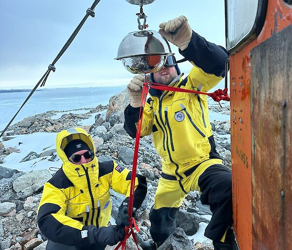 Two antarctic expeditioners in yellow survival clothing working on an installation.