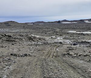 The image shows a rocky/dirt road into the distance. The horizon line features rocky hills against a blue sky.