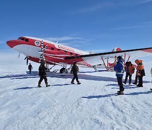 A group of expeditioners in front of a white and red plane on a white flat plain