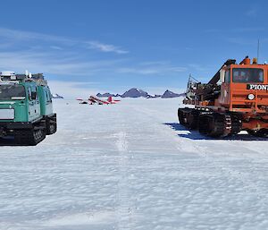 A green snow tractor on the left and an orange one on the right, on a flat snowy plain