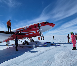 Pilot of the Basler on top of the wing while filling the tanks of the Basler while Mawson expeditioners look on and make them welcome