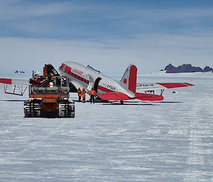 A snow tractor on the ice, refuelling a red and white ski plane