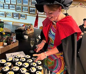 Graduate in robes and oversized bonnet looks at tray of cupcakes decorated as penguins