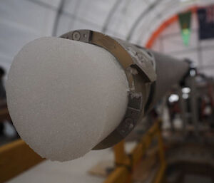 A cylinder of ice poking out the end of a metal drill barrel