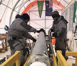 Two men beside a horizontal metal drill barrel with a small piece of ice core sticking out one end