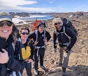 Four expeditioners smile at the camera on a rocky hill