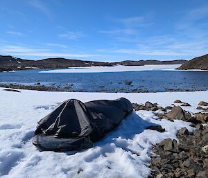 A black tent on snow in front of a lake