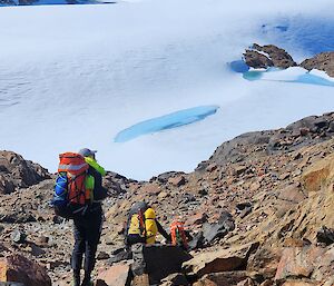 People walking over rocks towards a snowy slope and hills