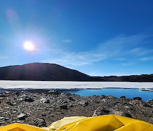 A yellow bivvy bag, blue sky, snow and a blue lake