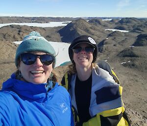 Two female expos smile at the camera with rocky hills in the background
