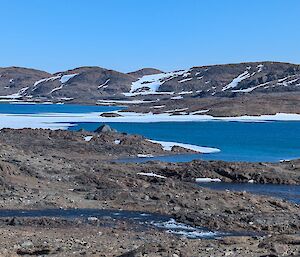 A blue lake surrounded by brown rocky hills and some snow