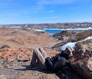 A person lies on a rock looking out over the snow lanscape with a lake in the distance