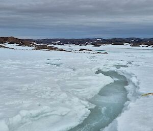 Water cuts a channel through snow, with a yellow pack in the foreground