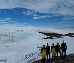 Wide shot of five people against a snowy background, with a blue glinting glacier