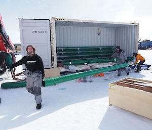 Two men moving a long metal pipe from a shipping container in the snow