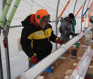 A man standing beside a long white ice core which is sitting in a v-shaped metal channel.