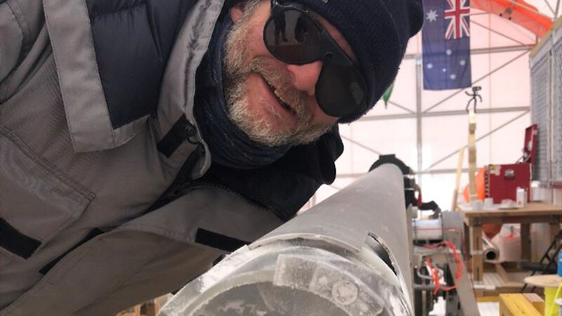 A man leaning over an ice core inside the metal barrel of an ice drill