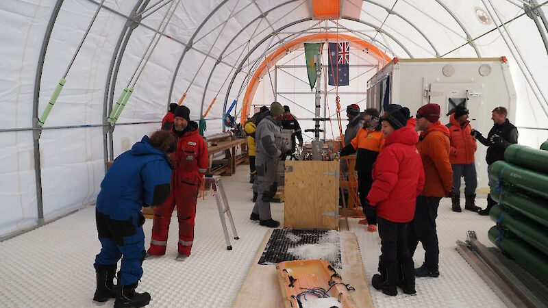 A group of people inside a semi-circular tent looking at an ice core drill