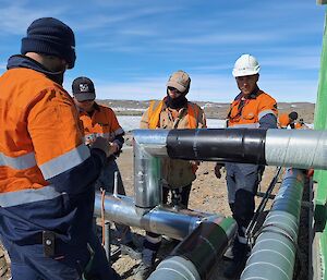 A group of hi vis people working on a large pipe attached to a green building