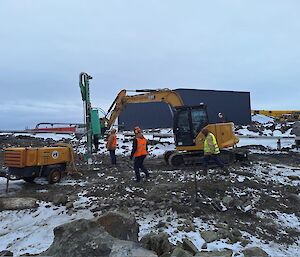 Diggers and construction work on a snowy rocky flat area with people in hi vis