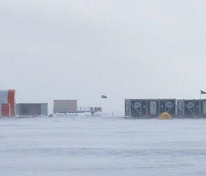 A series of shipping container buildings and two long, semi-circular tents in an icy landscape