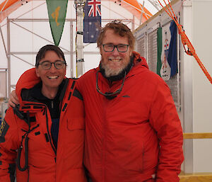 Two men in red freezer suits standing side by side inside a large drill tent