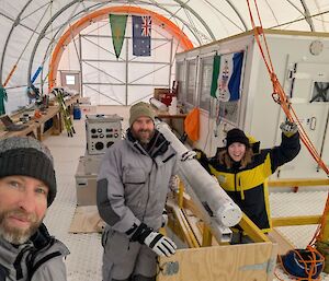 Three people standing beside an ice core drill reamer inside a large semi-circular drill tent.