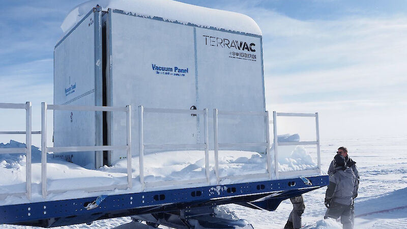 A large white freezer box sitting on a sled, covered in snow