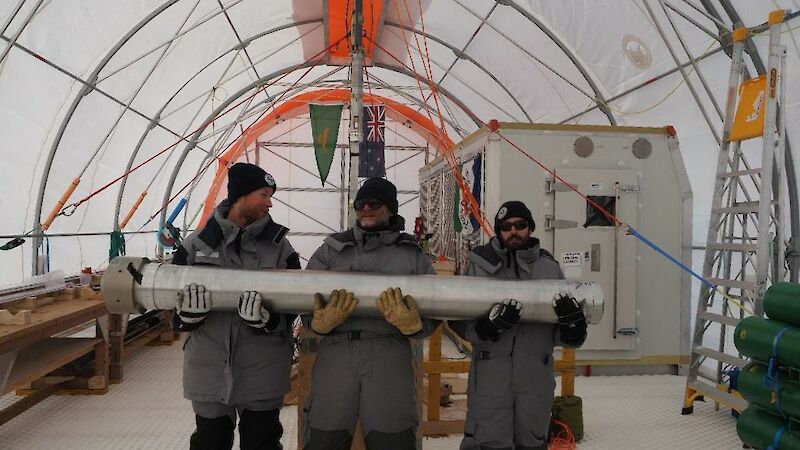 Three men holding a large metal cylinder