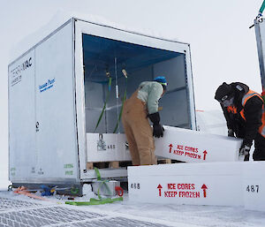 Two men loading rectangular white boxes filled with ice cores in to the back of a large insulated box.