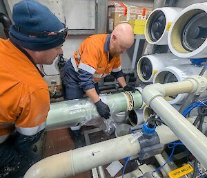 Two men fitting a new filter pipe to a machine