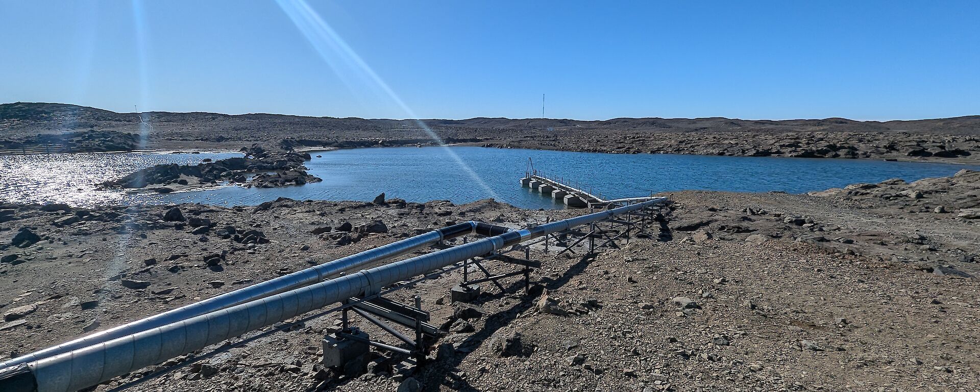 Metal pipes raised above gravelly ground, leading to a body of water.