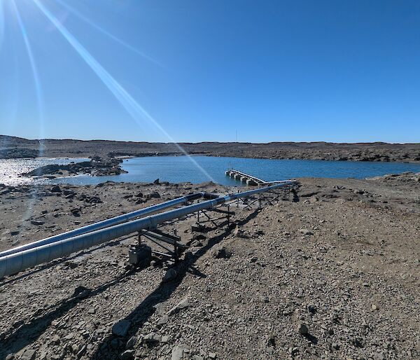 Metal pipes raised above gravelly ground, leading to a body of water.