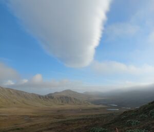 A large thick, inverted cone-shaped cloud over a rugged plain